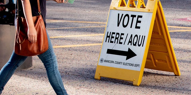A resident walks past a "vote here" sign outside a polling location at the Burton Barr Central Library in Phoenix, Ariz., Aug. 27, 2018.
