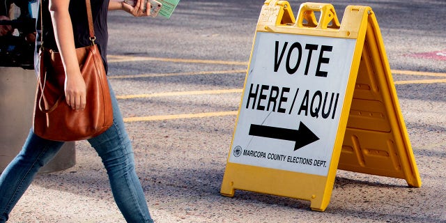 A resident walks past a "Vote Here" sign outside a polling location at the Burton Barr Central Library in Phoenix, Arizona, U.S.