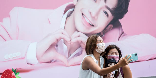 Two women take a selfie in front of a billboard showing a portrait of Anson Lo, a member of Cantopop boy band "Mirror," in Hong Kong.