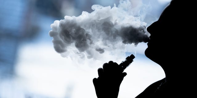 A young woman is showing smoking an e-cigarette. People need to break their routines in order to change their habits.