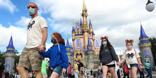 A masked family walks past Cinderella Castle in the Magic Kingdom, at Walt Disney World in Lake Buena Vista, Fla., on Monday, Dec. 21, 2020. 