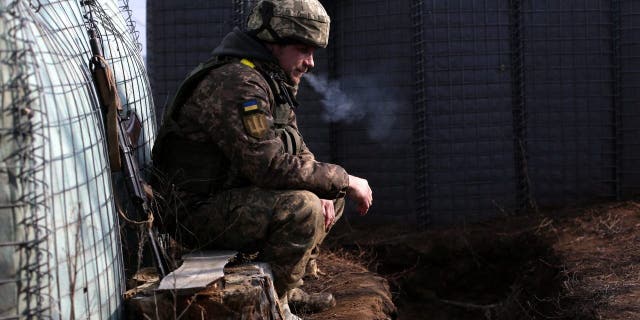 Ukrainian military personnel smoke in frontline positions with Russian-backed separatists on February 22, 2022, near the Troitsuke settlement in the Lugansk region.