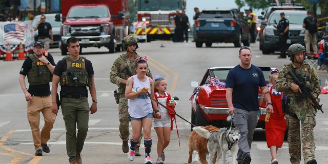 HIGHLAND PARK, ILLINOIS - JULY 04: Law enforcement escorts a family away from the scene of a shooting at a Fourth of July parade on July 4, 2022 in Highland Park, Illinois.  Police have detained Robert "Bobby" E. Crimo III, 22, in connection with the shooting in which six people were killed and 19 injured, according to published reports.  