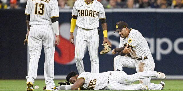 Jurickson Profar, #10 of the San Diego Padres (C), lies on the ground as Manny Machado, #13 (L), C.J. Abrams, #77, and Trent Grisham, #2, look on during the fifth inning of a baseball game against the San Francisco Giants July 7, 2022 at Petco Park in San Diego, California. Profar was injured on the play.