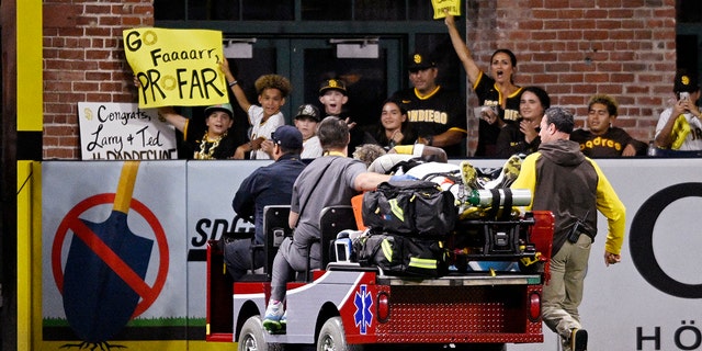 Fans hold signs as the San Diego Padres' #10 Jurikson professor is carried in a carriage during the fifth inning of a baseball game against the San Francisco Giants on July 7, 2022 at Petco Park in San Diego, California.  Proffer was injured during a collision with CJ Abrams, #77 of the San Diego Padres. 