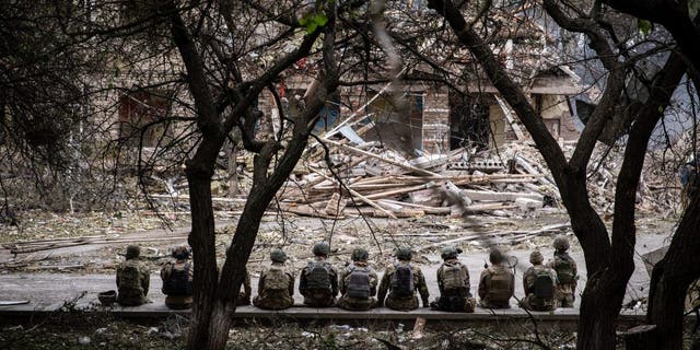 Украинские военные сидят на месте обстрела разрушенной школы в Краматорске.
