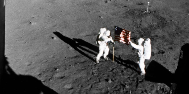 Astronaut Neil A. Armstrong stands on the left at the flag's staff. Astronaut Edwin E. Aldrin Jr. is also pictured. Picture was taken by the 16mm Data Acquisition Camera (DAC) mounted in the lunar module deploy flag.