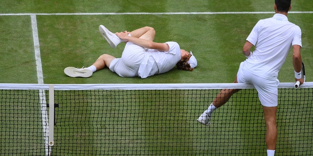 Novak Djokovic of Serbia climbs over the net to help Jannik Sinner of Italy after they slipped and fell during their Men's Singles Quarter Final match on day nine of The Championships Wimbledon 2022 at All England Lawn Tennis and Croquet Club on July 05, 2022 in London, England. 