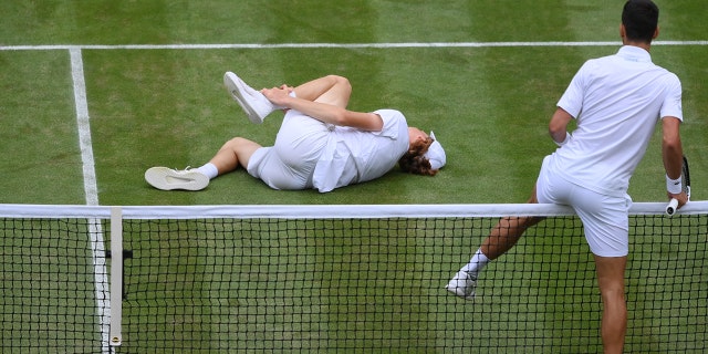 Novak Djokovic of Serbia climbs over the net to help Jannik Sinner of Italy after they slipped and fell during their Men's Singles Quarter Final match on day nine of The Championships Wimbledon 2022 at All England Lawn Tennis and Croquet Club on July 05, 2022 在伦敦, 英国.
