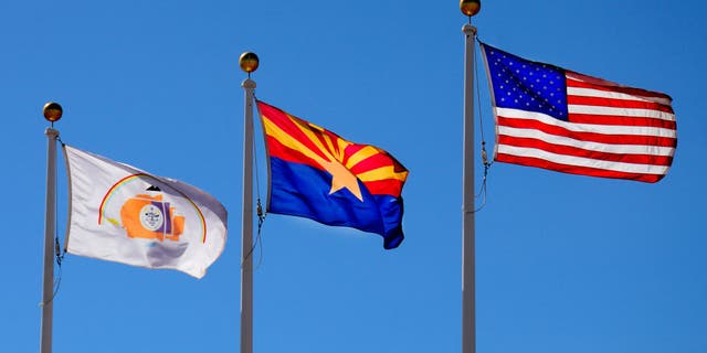 The Arizona state flag flies between the United States flag and the Navajo Nation flag.