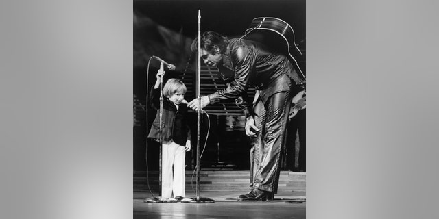 John Carter Cash (left), then three years old, became the youngest person to make a Las Vegas nightclub debut when he appeared on the stage of the Hilton and rendered "Mary Had a Little Lamb." Proud dad Johnny Cash holds the microphone for his son.