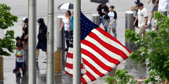 A United States flag flies at half-staff after a Fourth of July parade shooting in nearby Highland Park, Ill., while lines of fans wait to go through added security at Guaranteed Rate Field, Monday, July 4, 2022, in Chicago before a baseball game between the Chicago White Sox and the Minnesota Twins.