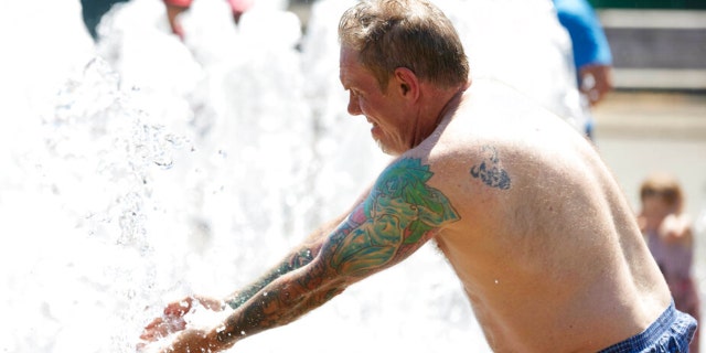 Matthew Carr cools off in the Salmon Street Springs fountain before returning to work cleaning up trash on his bicycle in Portland, Ore., Tuesday, July 26, 2022.