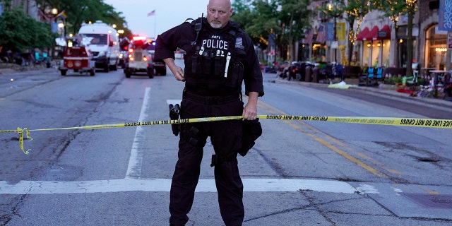 A police officer holds up police tape at the scene of a mass shooting at the Highland Park Fourth of July parade in downtown Highland Park, a Chicago suburb, on Monday, July 4, 2022.