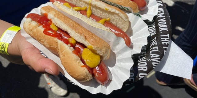 Person holding three hot dogs at event