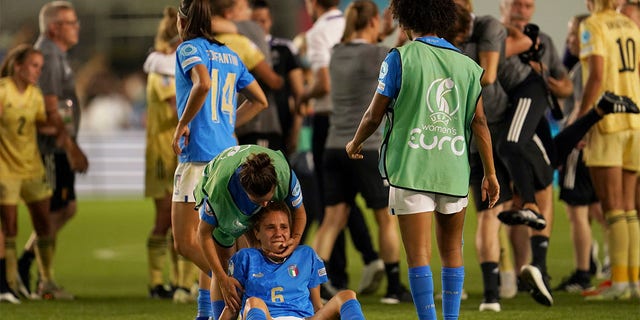 Italy's Manuela Giugliano, sitting on the ground, is comforted by a teammate at the end of the Women Euro 2022 group D soccer match between Italy and Belgium at the Manchester City Academy Stadium, in Manchester, England, Monday, July 18, 2022. Belgium won 1-0 to advance to the quarterfinals. 