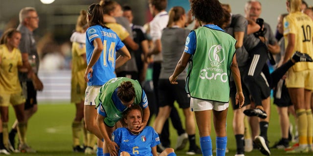Italy's Manuela Giugliano, sitting on the ground, is comforted by a teammate at the end of the Women Euro 2022 group D soccer match between Italy and Belgium at the Manchester City Academy Stadium, in Manchester, England, Monday, July 18, 2022. Belgium won 1-0 to advance to the quarterfinals.