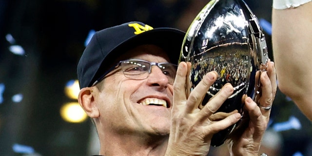 Michigan Wolverines coach Jim Harbaugh holds the trophy as he celebrates with his team after defeating the Iowa Hawkeyes in the Big Ten Football Championship Game on December 4, 2021 at Lucas Oil Stadium in Indianapolis, Indiana.