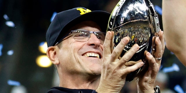Michigan Wolverines coach Jim Harbaugh holds the trophy as he celebrates with his team after defeating the Iowa Hawkeyes in the Big Ten Football Championship Game on December 4, 2021 at Lucas Oil Stadium in Indianapolis, Indiana.