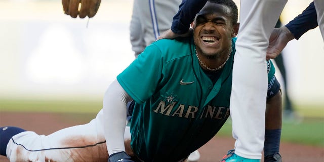 Seattle Mariners' Julio Rodriguez is helped up by third base coach Manny Acta after Rodriguez was tagged out at third by Toronto Blue Jays third baseman Matt Chapman after Rodriguez tripped on the way to third after hitting a double during the first inning of a baseball game, Friday, July 8, 2022, in Seattle.