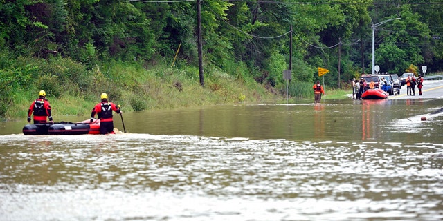 Members of the Winchester, Ky., Fire Department walk inflatable boats across floodwaters over Kentucky State Road 15 in Jackson, Ky., to pick up people stranded by the floodwaters.