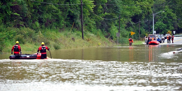 Members of the Winchester, Ky., Fire Department walk inflatable boats across floodwaters over Kentucky State Road 15 in Jackson, Ky., to pick up people stranded by the floodwaters.