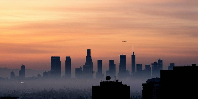 An airplane flies over the Los Angeles, California skyline as the sun rises on March 25, 2022. 