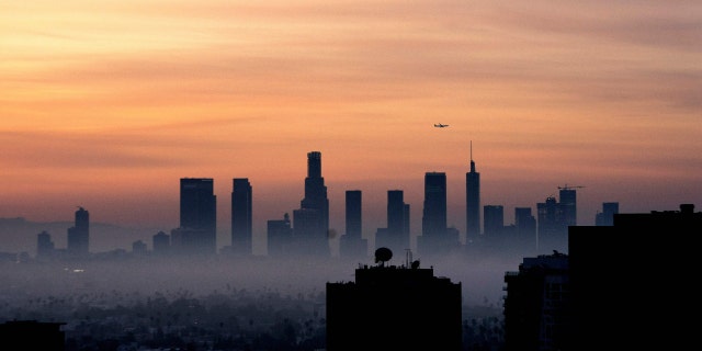 A plane flies over the Los Angeles, California, skyline at sunrise on March 25, 2022. 