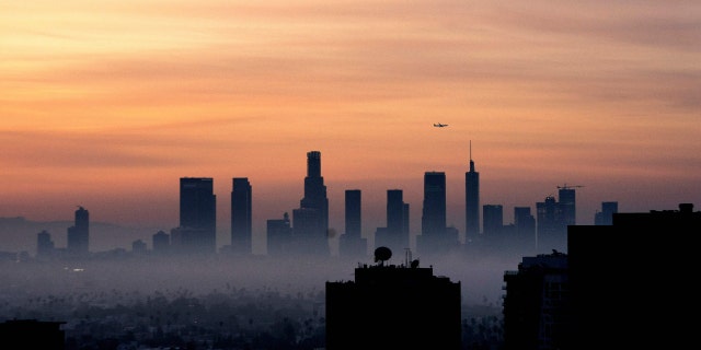 A plane flies over the Los Angeles, California, skyline at sunrise on March 25, 2022.