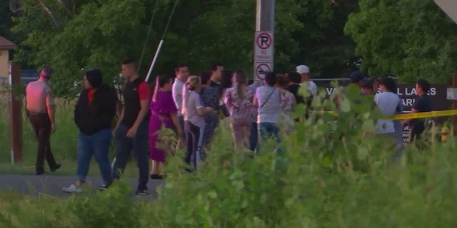A group of onlookers are seen near Vadnais Lake in Minnesota where officials fear a triple homicide involving young children took place Friday, July 1, 2022.