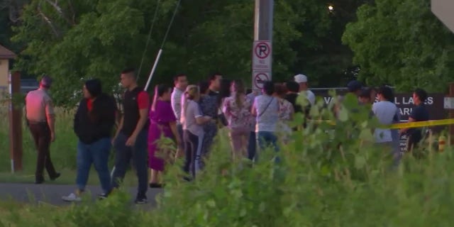 A group of onlookers are seen near Vadnais Lake in Minnesota where officials fear a triple homicide involving young children took place Friday, July 1, 2022.