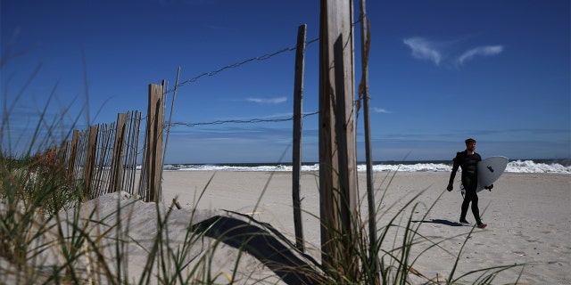 A man carries his surfboard after surfing in the Atlantic Ocean along the beach in Long Beach, New York, May 9, 2022. 