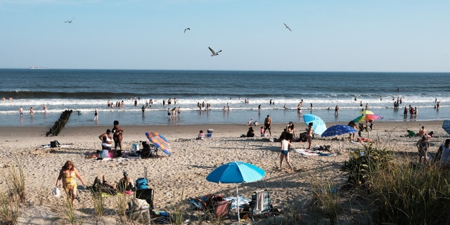 People enjoy a warm evening at Rockaway Beach on July 19, 2022 in New York City. Temperatures in New York City, and much of the East Coast, will rise into the 90s tomorrow as a heat wave blankets the area and much of the nation. Rockaway beaches were briefly closed today due to shark sightings close to the beach.