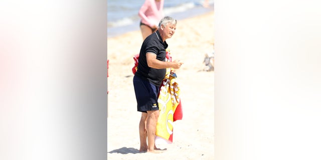 Alec Baldwin carried a massive, colorful beach towel, and wore a black polo shirt.