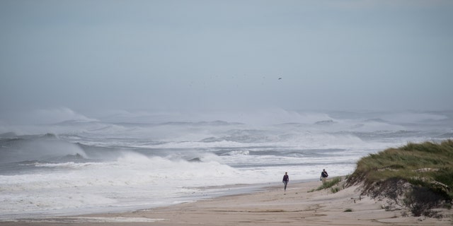 People walk along the beach as high waves produced by Hurricane Jose crash along the beach on Sept. 20, 2017 at Long Island's Smith's Point Beach in Shirley, New York.