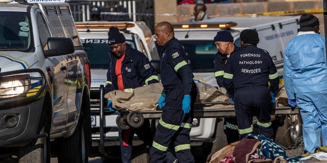 A body is removed from the scene of an overnight bar shooting in Soweto, South Africa, Sunday July 10, 2022. A mass shooting at a tavern in Johannesburg's Soweto township has killed 15 people.