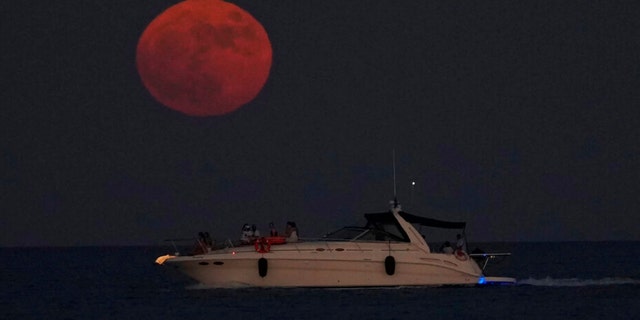 The full moon rises over the Mediterranean sea as people on a boat enjoy, in southern coastal city of Larnaca, in the southeast island of Cyprus, on Wednesday, July 13, 2022. 