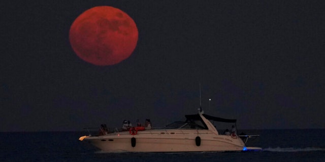 The full moon rises over the Mediterranean sea as people on a boat enjoy, in southern coastal city of Larnaca, in the southeast island of Cyprus, on Wednesday, July 13, 2022.