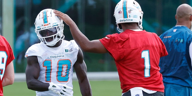 Tua Tagovailoa, #1, taps the helmet of Tyreek Hill, #10 of the Miami Dolphins, between drills during the Miami Dolphins Mandatory Minicamp at the Baptist Health Training Complex on June 1, 2022 in Miami Gardens, Florida.