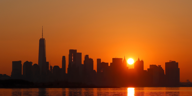 The sun rises behind lower Manhattan and One World Trade Center as a heatwave continues in New York City on July 23, 2022, as seen from Jersey City, New Jersey. 