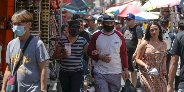 Shoppers with and without masks are shown at the crowded market on Santee Alley in Los Angeles.