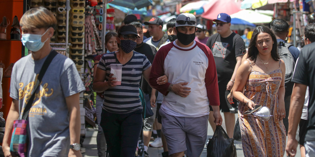 المتسوقون الذين يرتدون أقنعة وبدون أقنعة يظهرون في السوق المزدحمة في Santee Alley في لوس أنجلوس.