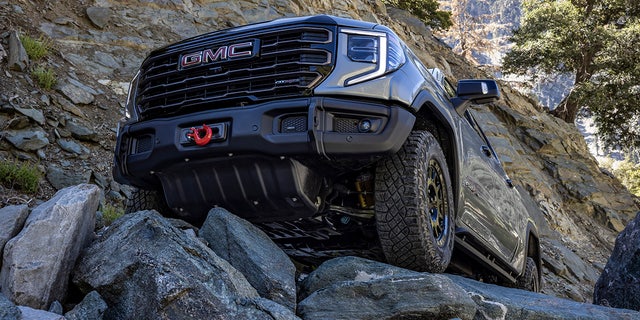 The 2023 GMC Sierra 1500 AT4X AEV Edition maneuvering over off-road rocks. The AEV Edition includes a winch-capable front bumper and five boron-steel underbody skid plates.