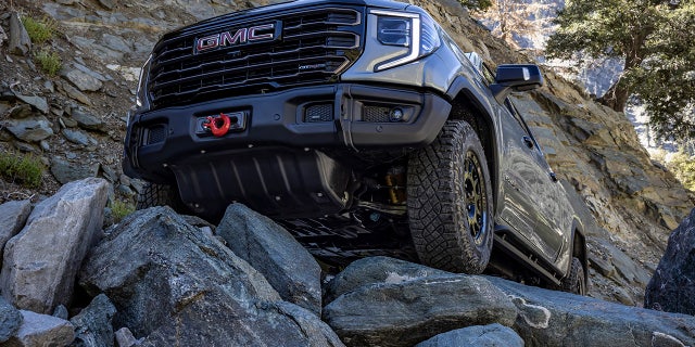 The 2023 GMC Sierra 1500 AT4X AEV Edition maneuvering over off-road rocks. The AEV Edition includes a winch-capable front bumper and five boron-steel underbody skid plates.