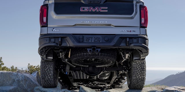 The 2023 GMC Sierra 1500 AT4X AEV Edition traveling off-road in the mountains. The AEV Edition features AEV branding throughout the vehicle as well as a black contrast inner tailgate. Also included is a full-size spare 33-inch Goodyear Wrangler Territory MT tire.