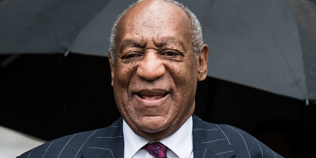 Bill Cosby smiles in a patterned suit jacket and purple tie outside the courthouse in Pennsylvania