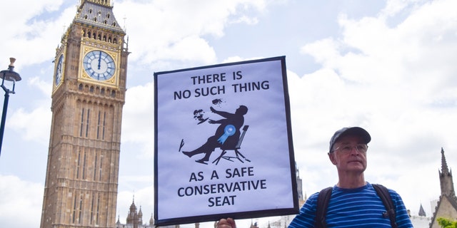 LONDON, UNITED KINGDOM - 2022/07/06: A protester holds a placard mocking the Conservative Party during the demonstration outside Parliament. Anti-Boris Johnson protesters gathered in Westminster as numerous ministers resigned from the Tory Government and pressure piles on Johnson to resign. (Photo by Vuk Valcic/SOPA Images/LightRocket via Getty Images)