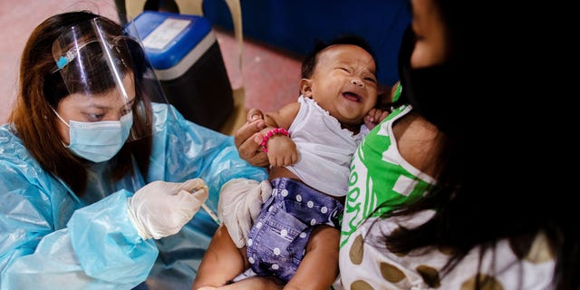 A nurse wearing personal protective equipment (PPE) to protect against coronavirus disease (COVID-19) administers standard vaccines to a child held by his mother at a local health center in Manila, Philippines January 27, 2021. 
