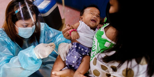 A nurse wearing personal protective equipment (PPE) to protect against coronavirus disease (COVID-19) administers standard vaccines to a child held by his mother at a local health center in Manila, Philippines January 27, 2021.