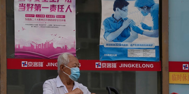 An old man in a mask is waiting near a poster promoting vaccination in Beijing on Tuesday, July 19, 2022.